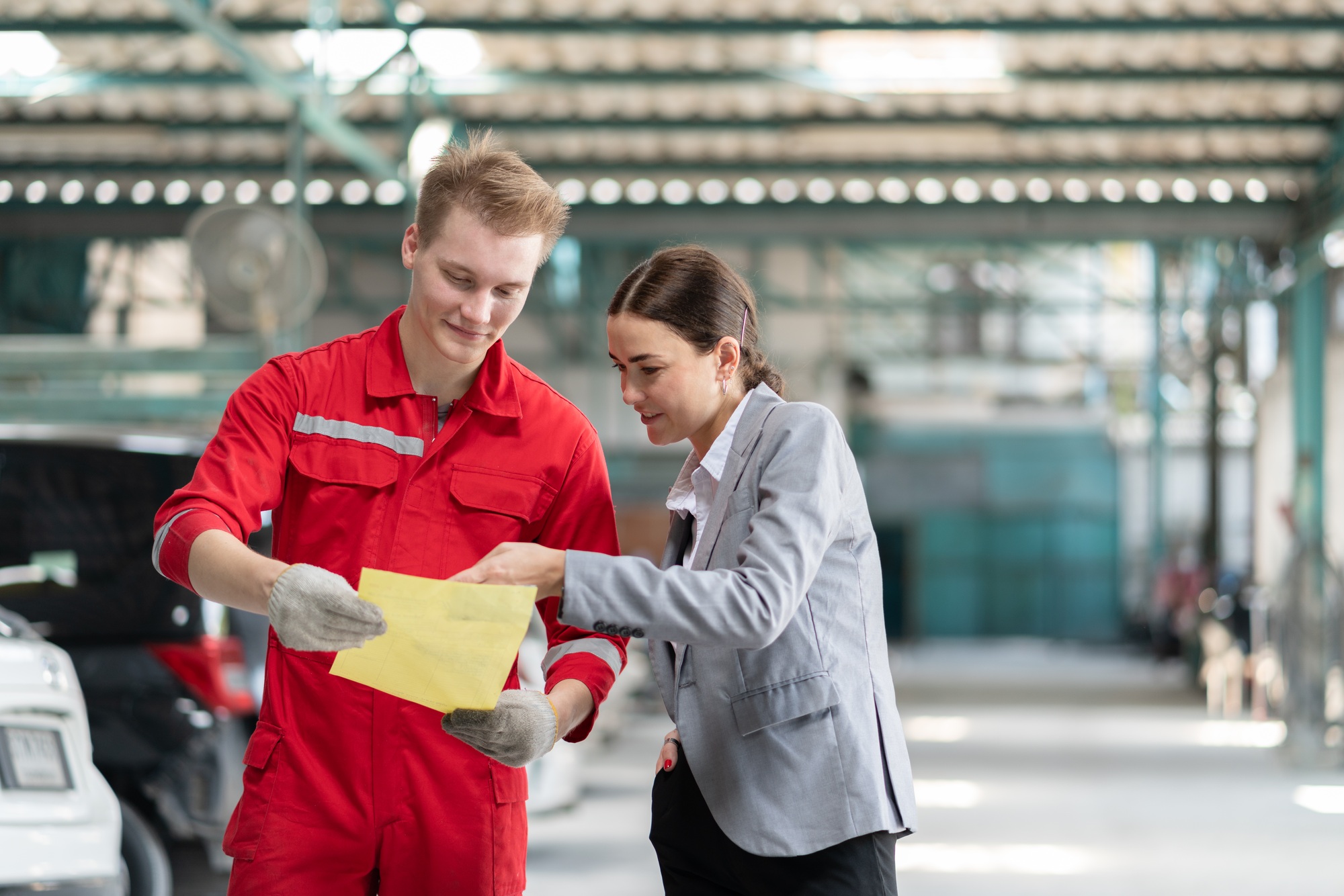 Male mechanic and female customer discussing car repairs and bills at garage